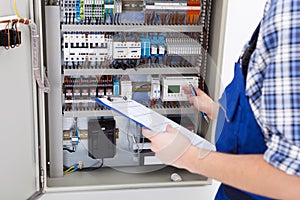 Technician holding clipboard while examining fusebox