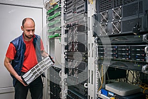 The technician is holding a stack of switches in his hands for installation in a server rack. A man works in a data center. A