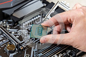 A technician holds the CPU Intel against the background of the motherboard Gigabyte. Computer parts. PC assembly concept