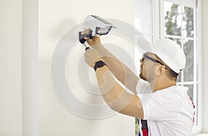 Technician installing a modern security camera on the wall inside a house or office