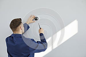 Technician installing modern surveillance CCTV dome camera on wall inside the house