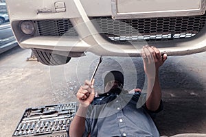 The technician lies flat under the car to inspect and fix the car holding a repair tool.Concept of service via insurance system at