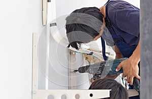 Technician man with hammerdrill installing an air conditioning in a client house, Young repairman fixing air conditioner unit,