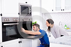 Technician In Overall Fixing Oven In Kitchen