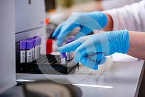 Technician placing blood tubes in the laboratory centrifuge. Selective focus on hands in blue latex gloves. Closeup.