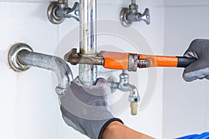 Technician plumber using a wrench to repair a water pipe under the sink.