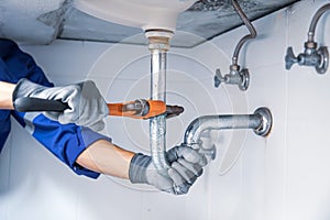 Technician plumber using a wrench to repair a water pipe under the sink. Concept of maintenance, fix water plumbing leaks, replace