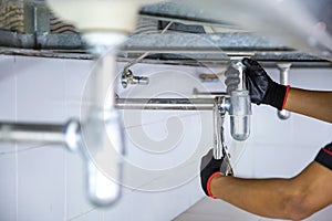 Technician plumber using a wrench to repair a water pipe under the sink. Concept of maintenance, fix water plumbing leaks, replace