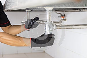 Technician plumber using a wrench to repair a water pipe under the sink. Concept of maintenance, fix water plumbing leaks, replace