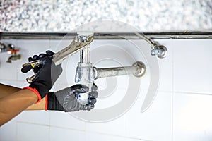 Technician plumber using a wrench to repair a water pipe under the sink. Concept of maintenance, fix water plumbing leaks, replace