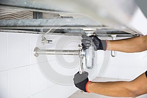 Technician plumber using a wrench to repair a water pipe under the sink. Concept of maintenance, fix water plumbing leaks, replace