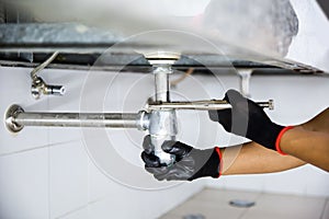 Technician plumber using a wrench to repair a water pipe under the sink. Concept of maintenance, fix water plumbing leaks, replace