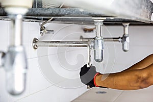 Technician plumber using a wrench to repair a water pipe under the sink. Concept of maintenance, fix water plumbing leaks, replace