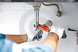 Technician plumber using a wrench to repair a water pipe under the sink. Concept of maintenance, fix water plumbing leaks, replace