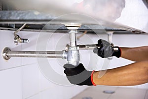 Technician plumber using a wrench to repair a water pipe under the sink. Concept of maintenance, fix water plumbing leaks, replace