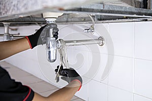 Technician plumber using a wrench to repair a water pipe under the sink. Concept of maintenance, fix water plumbing leaks, replace