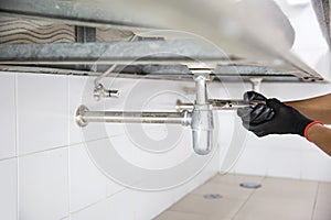 Technician plumber using a wrench to repair a water pipe under the sink. Concept of maintenance, fix water plumbing leaks, replace