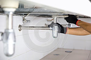 Technician plumber using a wrench to repair a water pipe under the sink. Concept of maintenance, fix water plumbing leaks, replace