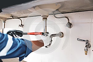 Technician plumber using a wrench to repair a water pipe under the sink. Concept of maintenance, fix water plumbing leaks, replace