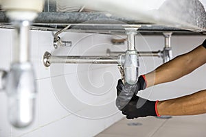 Technician plumber using a wrench to repair a water pipe under the sink. Concept of maintenance, fix water plumbing leaks, replace