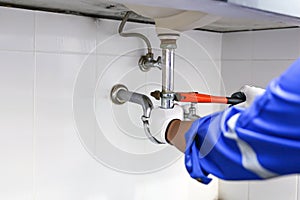 Technician plumber using a wrench to repair a water pipe under the sink. Concept of maintenance, fix water plumbing leaks, replace