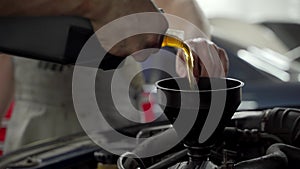 Technician pours new synthetic oil into car engine through funnel. Auto service worker performs regular maintenance