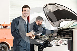 Technician Preparing Checklist While Colleague Inspecting Car In