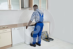 Technician Pulling Washing Machine In Kitchen