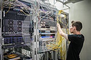A technician puts fiber optic internet cables in a server room. A young specialist works with communication wires in a data center