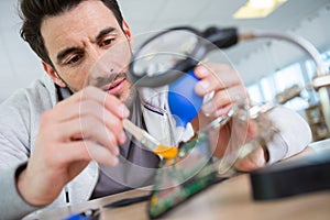 technician repairing electronics components through magnifying glass