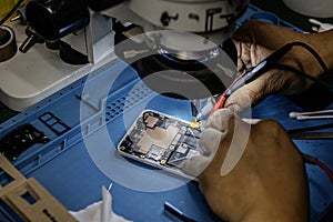 A technician repairing a mobile phone under a magnifying microscope on his blue work table against electromagnetic interference