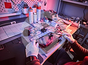 The technician repairs a broken tablet computer in a repair shop. Illumination with red and blue lights