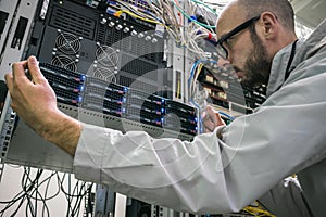 Technician repairs the central router in the datacenter server room. System administrator installs a new server in a modern data