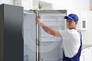 Technician with screwdriver repairing refrigerator in kitchen