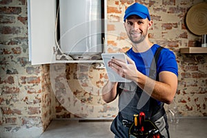 The technician servicing the water heater. A man checks the boiler room equipment using a tablet