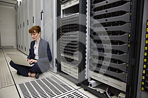 Technician sitting on floor beside server tower using laptop