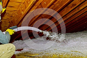 Technician spraying blown Fiberglass Insulation between Attic Trusses foam insulation construction foam from the gun to the roof