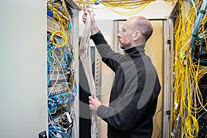 A technician stacks a wiring harness in a server room. A man works with communication cables in a data center. The signalman fixes