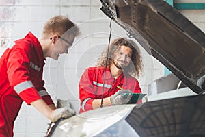 Technician team checking modern car at garage, Young Caucasian car mechanic with a checklist, Mechanics in uniform are working in