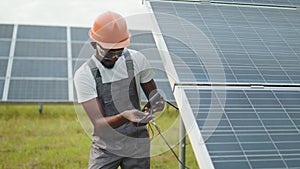 Technician in uniform using multimeter while checking voltage in solar panels. African american controlling production