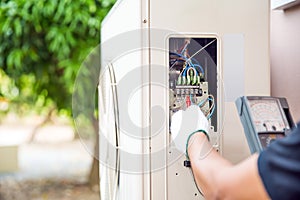 Technician using measuring equipment checking electric at circuit breaker on outdoor air compressor