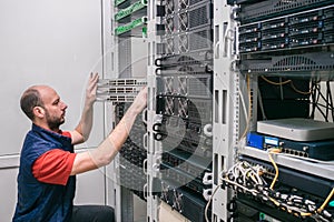 Technician was crouched down near computer racks. Engineer installs new switches in the server room. A man sets up server hardware