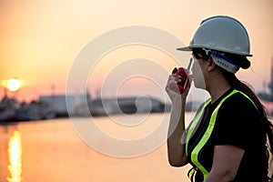 Technician woman sitting by the shipping port in the sunset, are using  radio communication