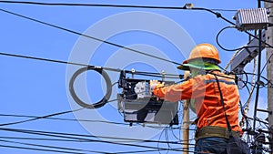 Technician on wooden ladder is working to install fiber optic and splitter box on power pole against blue sky