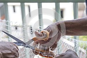 technician worker man install use orange scissors cut plastic net for protect pigeon bird in balcony apartment. Professional