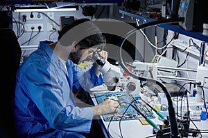 Technician working on circuit board under microscope in lab