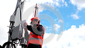 Technician working on roof near the antenna, engineer male in a protective vest and hardhat writes notes in notebook on