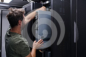 IT technician installing server hardware in a data center server rack performing maintenance and network setup