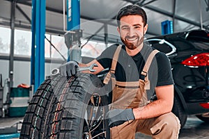 A technician in workwear, holding a wrench and a car tire in tire fitting