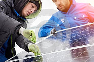 Technicians in blue suits mounting photovoltaic solar panels on roof of modern houses.